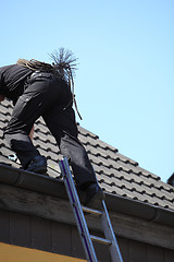 Image showing Chimney sweep climbing onto the roof of a house