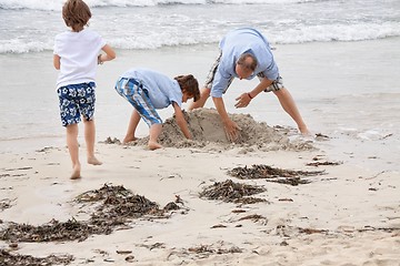 Image showing father and sons on the beach playing in the sand