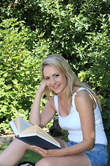 Image showing Pretty smiling woman reading in the garden