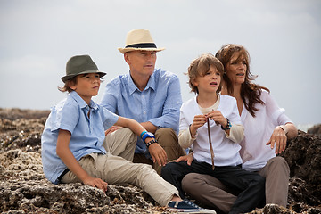 Image showing happy family sitting on rock and watching the ocean waves