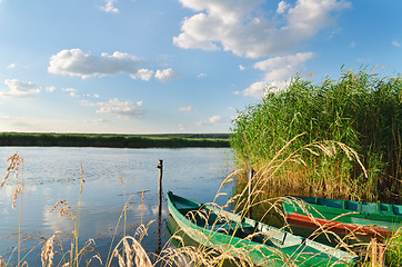 Image showing beautiful river and old boats near green grass under cloudy sky