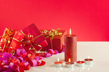Image showing Christmas gifts and candles over red background