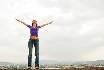 Image showing Young woman staying with raised hands against blue sky