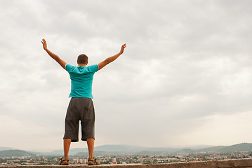 Image showing Young man staying with raised hands against blue sky