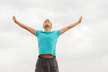 Image showing Young man staying with raised hands against blue sky