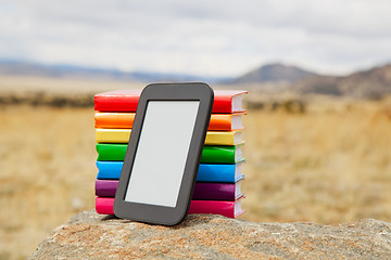 Image showing Stack of printed books with electronic book reader