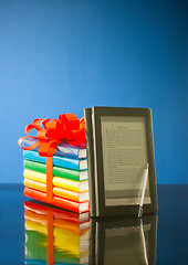 Image showing Stack of books with electronic book reader against blue background