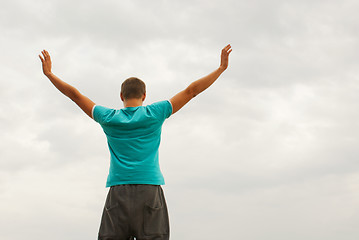 Image showing Young man staying with raised hands against blue sky