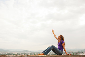 Image showing Young woman sitting with raised hand against blue sky