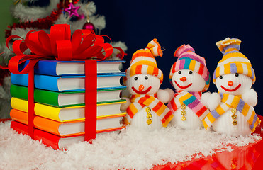 Image showing Stack of colorful books tied up with red ribbon and three snowme