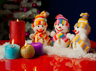 Image showing Three snowmen and burning candles over the blue background