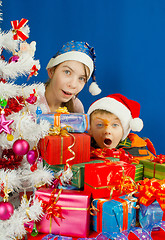 Image showing Two surprised kids looking from behind the Christmas presents