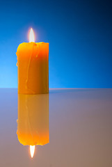 Image showing Burning yellow candle against blue background