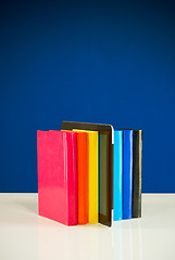 Image showing Row of colorful books and tablet PC over blue background