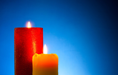 Image showing Two burning colourful candles against blue background