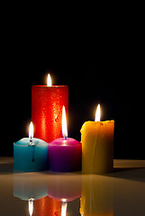 Image showing Four colourful burning candles against black background