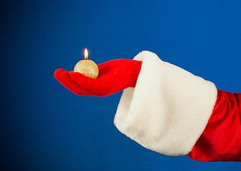 Image showing Santa's hand holding a burning candle over blue background