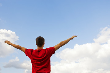 Image showing Young man staying with raised hands against blue sky