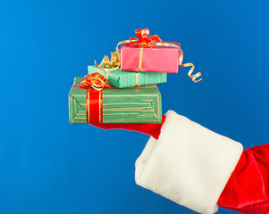 Image showing Santa's hand holding presents over blue background