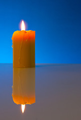 Image showing Burning yellow candle against blue background