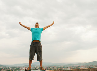 Image showing Young man staying with raised hands against blue sky