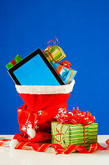 Image showing Tablet PC with heap of presents in red bag against blue backgrou
