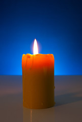 Image showing Burning yellow candle against blue background