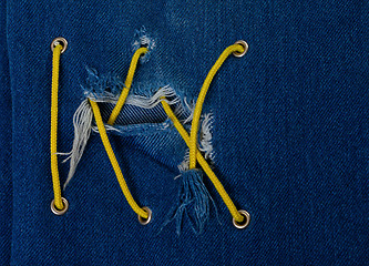 Image showing Blue jean with hole and crisscross yellow lacing