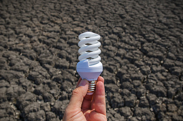 Image showing energy saving lamp in hand over drought earth