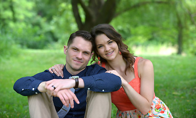 Image showing Happy young couple posing seated on the ground in a garden setti