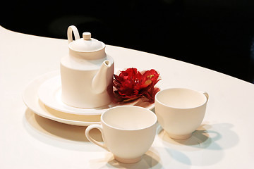 Image showing White teapot, cups and saucers with a red flower