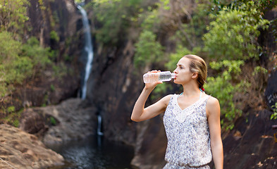 Image showing Young healthy woman drinks water from bottle.Outdoor