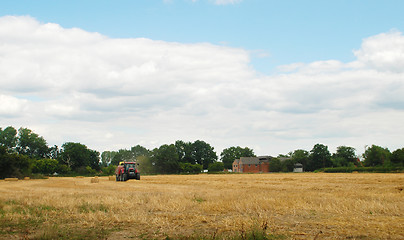 Image showing Red tractor baling straw in a farm field 