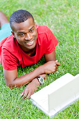 Image showing young smiling african student sitting in grass with notebook