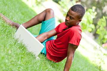 Image showing young smiling african student sitting in grass with notebook