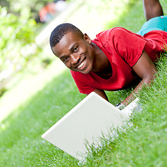 Image showing young smiling african student sitting in grass with notebook