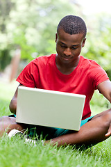 Image showing young smiling african student sitting in grass with notebook