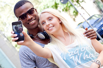 Image showing young smiling multiracial couple taking foto by smartphone 