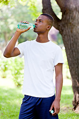 Image showing athletic african young man drinking water outdoor