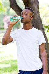 Image showing athletic african young man drinking water outdoor