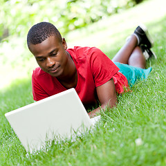 Image showing young smiling african student sitting in grass with notebook