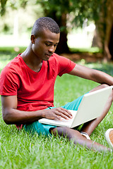 Image showing young smiling african student sitting in grass with notebook