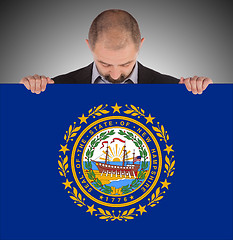 Image showing Smiling businessman holding a big card, flag of New Hampshire