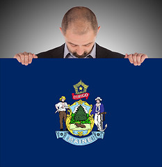 Image showing Smiling businessman holding a big card, flag of Maine