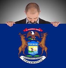 Image showing Smiling businessman holding a big card, flag of Michigan