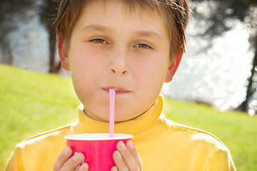 Image showing Young boy drinking strawberry milk outdoors
