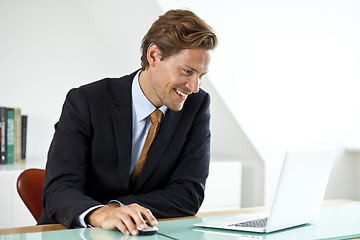 Image showing miling handsome businessman using laptop in office