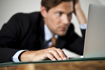 Image showing Businessman rests his head in one hand while working on laptop