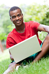 Image showing young smiling african student sitting in grass with notebook