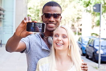 Image showing young smiling multiracial couple taking foto by smartphone 